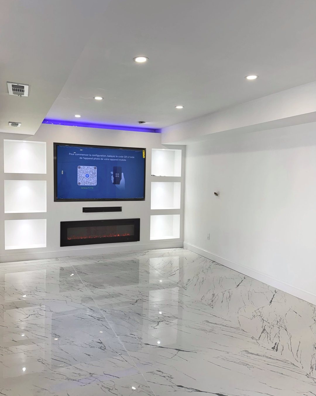 The same basement finished as a media room with marble-look tile, a lit built-in wall and an electric fireplace