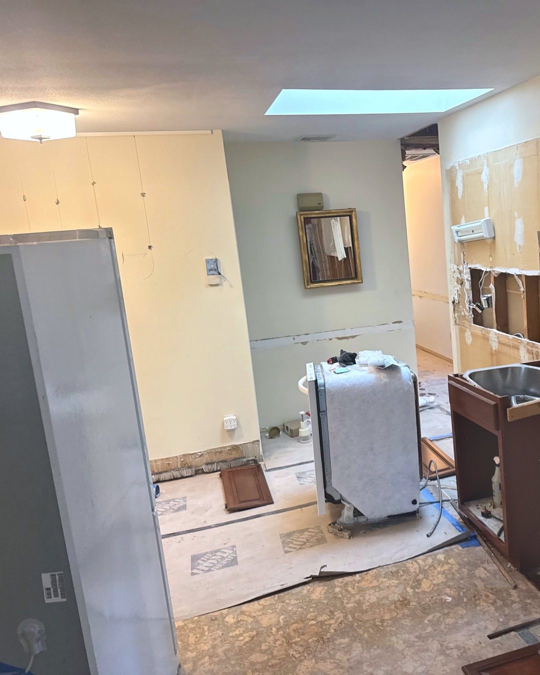 Kitchen during demolition: cabinets pulled out, drywall cut open, subfloor exposed