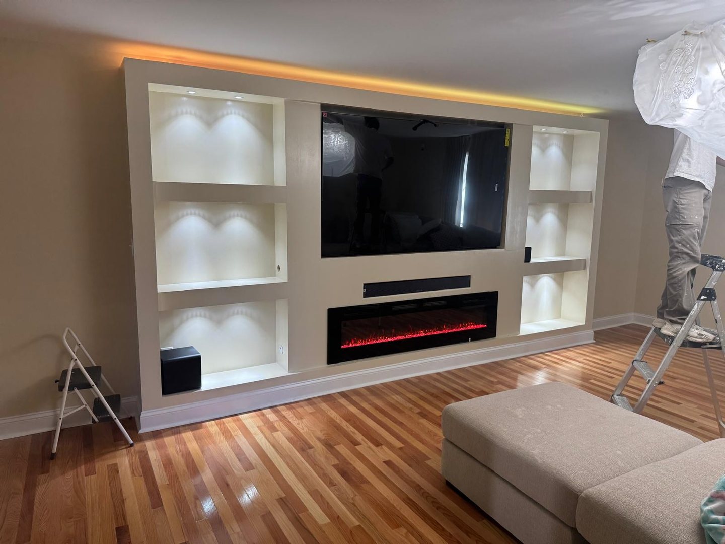 Finished built-in media wall with lit display niches, a recessed TV, soundbar and electric fireplace