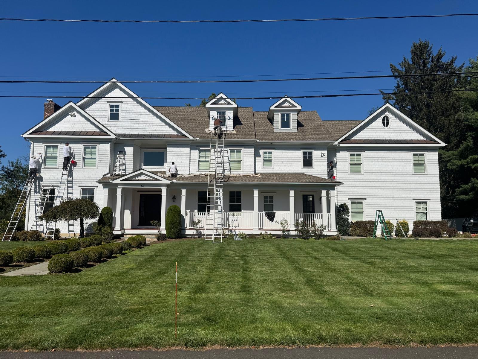 Five painters on ladders and the porch roof painting the front of the house